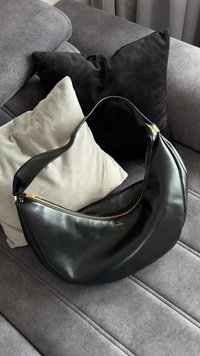 Borsa a tracolla in pelle nera con forma curva e tracolla lunga, caratterizzata da una chiusura con cerniera dorata e un marchio discreto sulla parte anteriore.