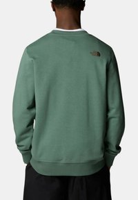 Felpa verde con finitura testurizzata, polsini a coste e scollatura arrotondata. Presenta un piccolo logo marrone sulla parte superiore della schiena.