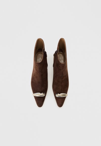 Brown suede ankle boots with a pointed toe and silver metal accent on the front. Features a side zipper for closure. Smooth inner lining.