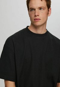 Svart t-shirt med kort ärm, tillverkad av textil med struktur, lös passform och rund halsringning. Har ett subtilt våffelmönster.