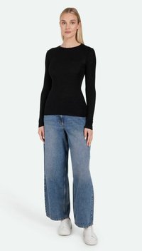 Schwarzes Langarmshirt aus glattem Material, kombiniert mit weit geschnittenen blauen Jeans und weißen Sneakern vor einem hellen Hintergrund.