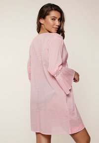 Różowa, lekka sukienka z długimi rękawami, ozdobiona koronkowymi akcentami i luźnym krojem. Teksturowana tkanina z wykończonym brzegiem i kwiatowym detalem na dole.