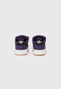 Des baskets en daim violet avec une semelle intermédiaire blanche, une semelle extérieure en caoutchouc caramel et un onglet de talon noir portant un logo blanc. Deux paires sont montrées de dos.