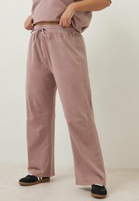 Ljust rosa, vida byxor med dragsko i midjan och sidsömmar, tillverkade av ett mjukt tyg. Matchas med svarta sneakers.