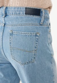 Svetle modré denimové džíny s zadní kapsou s kontrastním prošíváním a černou koženou nášivkou na pase s názvem značky.