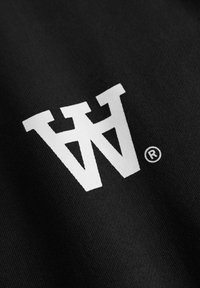 Tissu noir présentant un grand logo graphique blanc aux bords angulaires avec un symbole de marque déposée à droite.