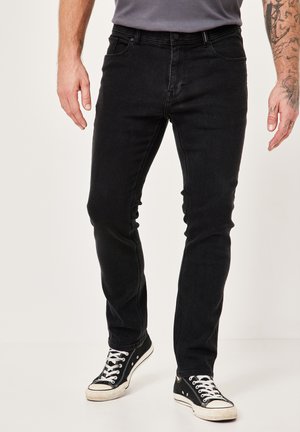 Schwarze Jeans aus Denim mit schlanker Passform, Fünf-Taschen-Design und dezentem Verblassen. Kombiniert mit schwarzen Sneakers aus Leinwandmaterial.