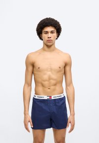 Μπλε ναυτικό μαγιό από ελαφρύ ύφασμα με ελαστική ζώνη μέσης που διαθέτει λωρίδα με λογότυπο. Το σχέδιο περιλαμβάνει κλείσιμο με κουμπί και πλαϊνές τσέπες.