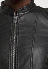 Giacca di pelle nera con colletto alto, zip argentata e dettagli cuciti lungo la parte anteriore per una maggiore texture e design.