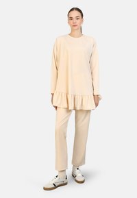 Beige sweatshirt met een gerimpelde zoom, gecombineerd met bijpassende broeken. Gladde stof met een ontspannen pasvorm en lange mouwen. Witte sneakers inbegrepen.