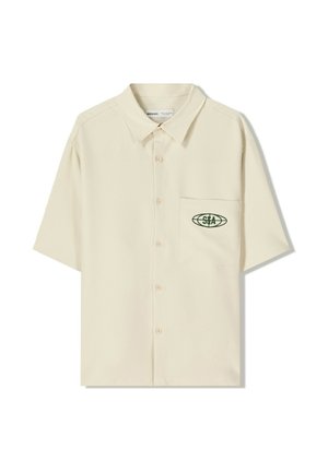 Chemise beige à manches courtes en tissu léger, dotée d'une poche poitrine avec un logo brodé vert et d'une fermeture à boutons sur le devant.