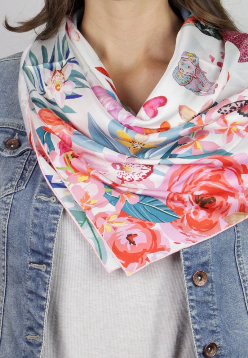 Femme portant un foulard floral coloré avec des fleurs roses, rouges et bleues sur un haut blanc et une veste en jean.
