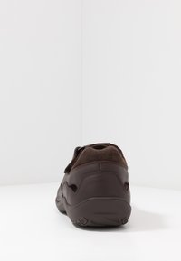 Braunes Leder-Schuh mit Oberschuh aus Wildleder, runder Form und verstellbarem Riemen. Sichtbare strukturelle Details und eine robuste Gummisohle.