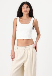 Hvit stripete crop top med firkantet hals og tykke stropper, sammen med løse, lys beige bukser med elastisk midje.