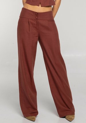 Pantalones de tiro alto y pierna ancha de color óxido con dos botones en la pretina, combinados con zapatos puntiagudos color beige.