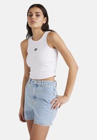 Weißes, geripptes Tanktop mit kleinem, schwarzem, sechseckigem Logo, kombiniert mit hellblauen, hochgeschnittenen Jeansshorts mit vorderen Taschen.
