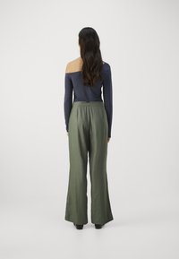 Haut bleu marine à manches longues et épaules dénudées, associé à un pantalon olive taille haute, à jambes larges. Tissu lisse avec une coupe décontractée.