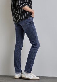 Mörkblå skinny jeans med ett lätt urblekt mönster, femfickorsdesign, matchat med vita sneakers med ljusblå accenter.