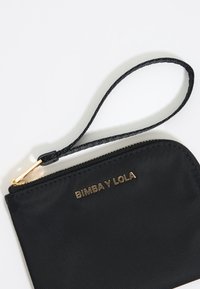 Borsa in tessuto nera con logo dorato "BIMBA Y LOLA". Dotata di chiusura con zip e di un manico a polso intrecciato. Texture liscia, forma rettangolare compatta.
