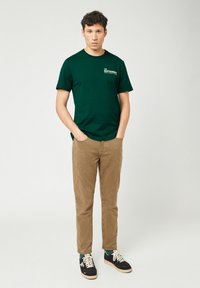 Groene katoenen T-shirt met korte mouwen en ronde hals, gecombineerd met beige corduroy broek en zwarte sneakers met witte veters.