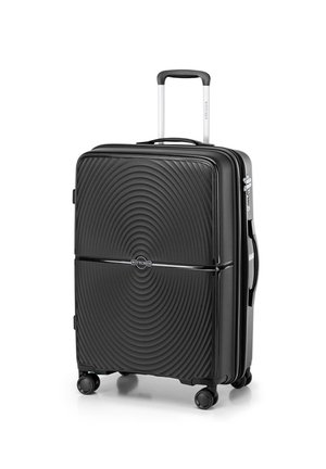 Valise rigide noire avec un motif en vagues circulaires, poignée rétractable et quatre roues noires pour la mobilité. Logo de la marque visible.