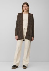 Brauner Strickcardigan mit offenem Vorderteil, langen Ärmeln und lockerer Passform, kombiniert mit einem leichten Hemd und beigen, weiten Hosen.