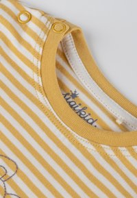 Gelb-weiß gestreifter Stoff mit rundem Ausschnitt, zwei runden gelben Druckknöpfen an der Schulter und einem gestickten Design.