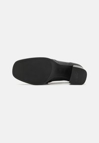 Sole di scarpa in pelle nera con superficie testurizzata e tacco basso a blocco. Presenta una finitura liscia e un design antiscivolo.