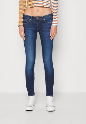 Slim-Fit blaue Jeans getragen mit weißen Plateau-Sneakern und einem langärmeligen Crop-Top mit horizontalen orange-, weißen und schwarzen Streifen.