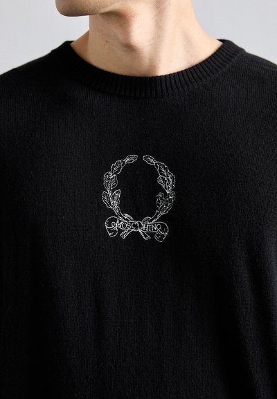 Svart stickad tröja med en vit broderad lagerkrans och "MOSCHINO"-text i mitten. Ribbad halsringning ger textur.