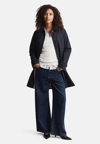 Tmavomodrý kabát na gombíky, textúrovaný krémový sveter, modrá pruhovaná košeľa, široké tmavé rifle, čierne podpätky. Tesný strih s viacvrstvovým vzhľadom.