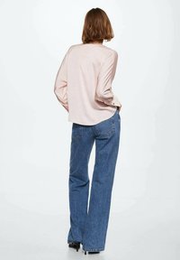 Camicia a maniche lunghe rosa pallido con vestibilità comoda e dettagli con bottoni sui polsini, abbinata a jeans in denim blu a vita alta, modello a gamba dritta.