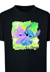Juodas marškinėliai su spalvinga dviejų animacinių personažų grafika. Fone matomi žali atspalviai, dobilai ir tekstas "Clover All Over".