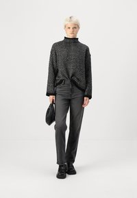 Schwarz-weiß gestreifter Rollkragenpullover im Fischgrätmuster, kombiniert mit dunkelgrauen geraden Jeans und klobigen schwarzen Schuhen. Schwarze Handtasche.