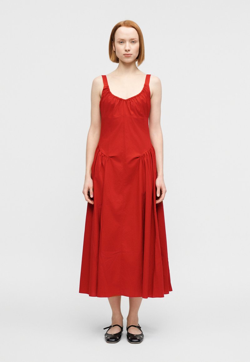 Κόκκινο βαμβακερό φόρεμα με εφαρμοστό μπούστο, φ αρδιές τιράντες και ραφές που συγκεντρώνονται στη μέση, καταλήγοντας σε φούστα πλήρους μήκους μέχρι τον αστράγαλο.