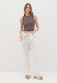 Top senza maniche a righe marroni e bianche abbinato a pantaloni bianchi larghi. L'outfit presenta una vestibilità rilassata e un tessuto leggero.
