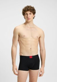 Boxer in cotone nero con un cinturino logo rosso, realizzati in un tessuto morbido ed elasticizzato. Il design presenta una forma aderente e nessun motivo visibile.