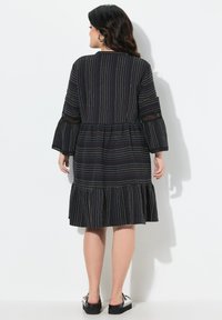 Robe noire avec des rayures multicolores verticales, des manches évasées et un ourlet à volants. Présente un col rond simple et un tissu texturé.