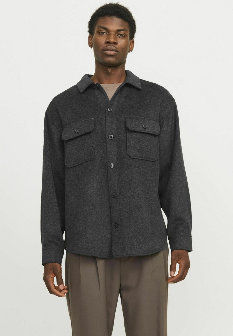 Camisa chaqueta de lana gris con cuello, dos bolsillos en el pecho y cierre de botones. Mangas largas con puños abotonados y un corte relajado.
