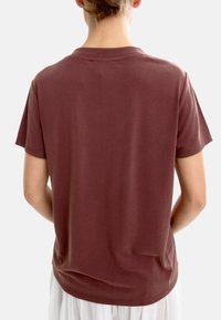 Bordowa koszulka z krótkim rękawem wykonana z miękkiej bawełny, z okrągłym dekoltem i luźnym krojem. Posiada płaskie szwy i gładką fakturę.