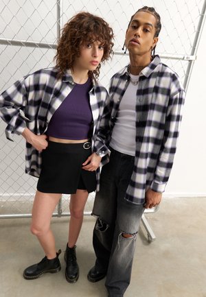 Prikkete lilla og hvite flanellskjorter båret over en lilla crop top og et svart omslagsskjørt. Svart combat-støvler og slitte jeans fullfører antrekket.