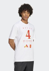 Hvit bomulls T-skjorte med rød tekst "REYES 4 DE EUROPA" med grafikk, Adidas-logo og en spansk flagg aksent. Korte ermer, rund hals.