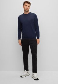 Navy sweatshirt with crew neck, ribbed cuffs, and subtle logo on chest, paired with black trousers and white sneakers with color accents.