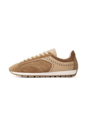 Brauner Sneaker aus Veloursleder und Leder mit niedrigem Schnitt, beigen Schnürsenkeln, genietetem Seitendetail und weißer Sohle auf weißem Hintergrund.