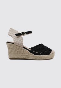 Sandale compensée tissée noire avec une sangle chevronnée beige et boucle ajustable. Présente un talon en jute et un design à bout ouvert.