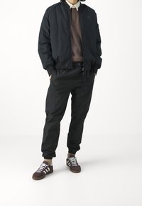 Svart lätt bomberjacka, brun polo shirt, svarta cargo byxor med dragkedjor och mörkröda sneakers med vita ränder.