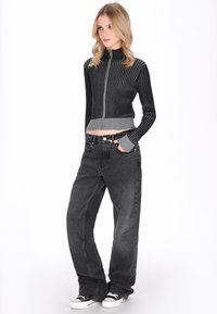 Fekete és szürke, rövidített, cipzárral ellátott pulóver függőleges bordázattal és hosszú ujjakkal; laza szabású sötétszürke farmerrel és fekete tornacipővel párosítva.