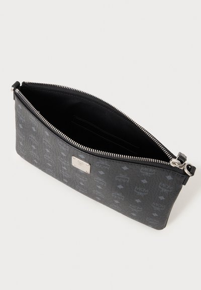 Pochette noire zippée avec plaque logo argentée, ornée de motifs répétant les logos MCM, et un dessus ouvert révélant un intérieur en tissu noir.
