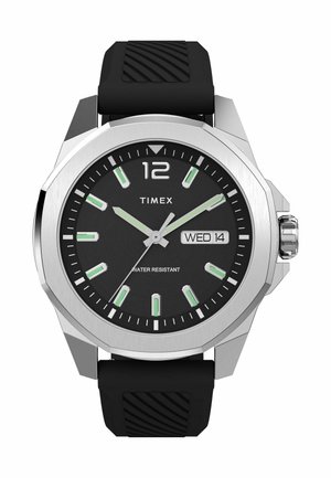 Montre Timex avec un cadran noir, un boîtier argenté et des marqueurs d'heure verts. Elle possède un bracelet en caoutchouc et affiche la date ainsi que la résistance à l'eau.