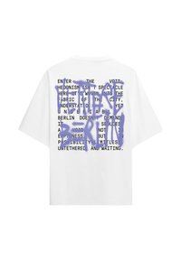 Maglietta oversize bianca con testo stampato nero e grande graffiti viola spray con la scritta "I WANT BERLIN" sul retro.